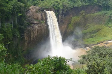 A powerful tropical waterfall cascading down a rocky cliff into a misty pool surrounded by lush green jungle.