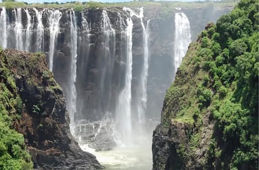 Panoramic view of Victoria Falls cascading into a rocky gorge surrounded by lush green cliffs.