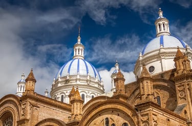 The blue and white tiled domes of the New Cathedral in Cuenca, Ecuador against a cloudy sky.