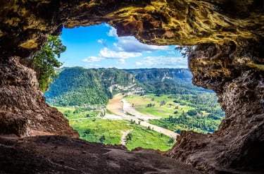 Panoramic view of a tropical river valley and green mountains seen from inside a dark rock cave.