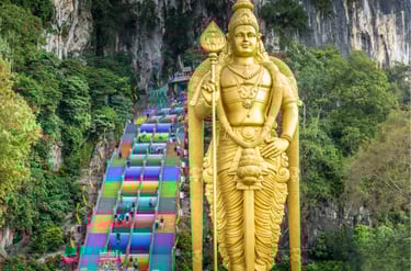 Golden Lord Murugan statue standing before the colorful rainbow stairs at Batu Caves in Malaysia.