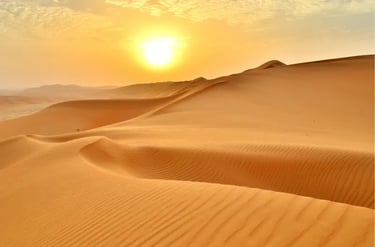 Golden sunset over rolling orange sand dunes in the vast desert landscape.