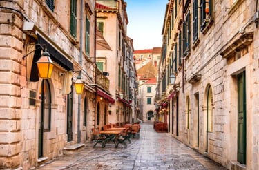Empty outdoor restaurant seating in a narrow stone alleyway in Dubrovnik Old Town, Croatia.