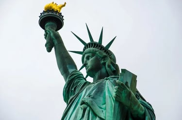 A low-angle view of the Statue of Liberty holding a golden torch against a gray sky in New York.