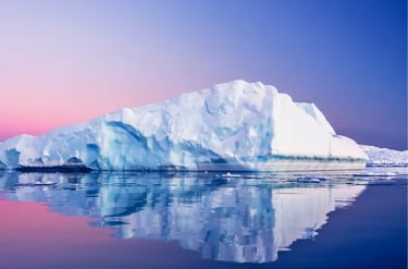 Large white iceberg reflecting in calm Antarctica waters during a pink and blue sunset.