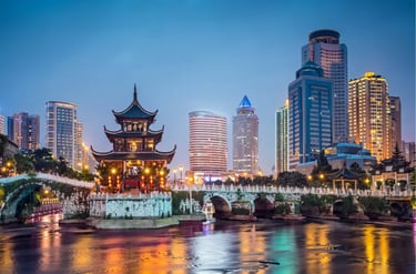 The Jiaxiu Pavilion and arched bridge at dusk in Guiyang, China with a modern city skyline backdrop.