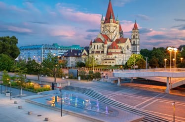 St. Francis of Assisi Church in Vienna, Austria, at sunset with a modern fountain and pink clouds.