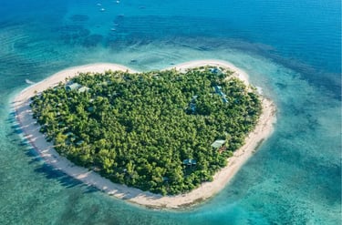 Aerial view of a heart-shaped tropical island resort in Fiji surrounded by clear blue ocean water.