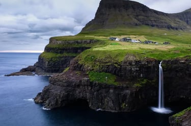 Mulafossur Waterfall cascading from green cliffs into the ocean near Gasadalur village, Faroe Islands.