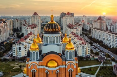 Golden-domed Orthodox cathedral overlooking the Kyiv city skyline and residential buildings at sunset.