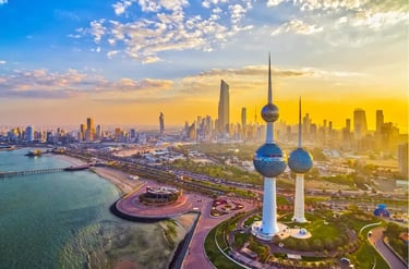 Aerial view of Kuwait Towers and Kuwait City skyline at golden hour sunset along the Persian Gulf coast.
