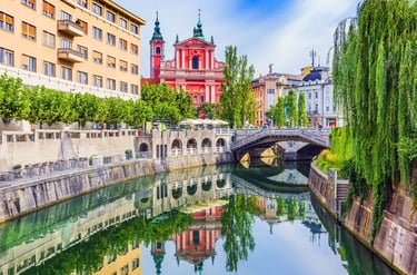 The pink Franciscan Church of the Annunciation reflected in the Ljubljanica River at Triple Bridge, Ljubljana.