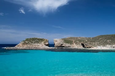 Turquoise waters of the Blue Lagoon in Comino, Malta, with limestone cliffs under a blue sky.
