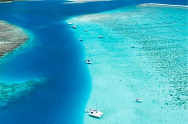 Aerial view of sailboats anchored in a crystal clear turquoise lagoon with tropical coral reefs.