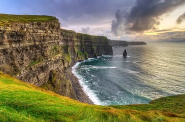 Panoramic view of the Cliffs of Moher in Ireland at sunset with green grass and crashing waves.
