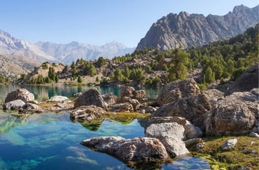 Crystal clear blue mountain lake with jagged rocks and pine trees in the Fann Mountains of Tajikistan.