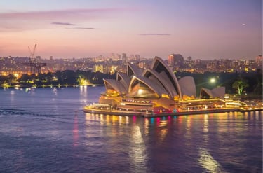 The Sydney Opera House illuminated at dusk with city lights reflecting in the harbor water.