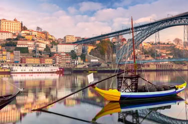 Traditional Rabelo boats on the Douro River with the Dom Luís I Bridge and Porto city skyline in Portugal.