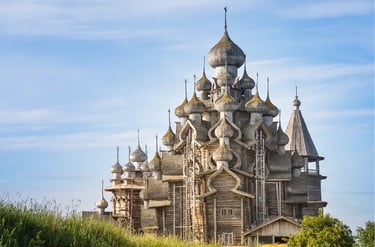 The historic wooden Church of the Transfiguration on Kizhi Island with multiple onion domes under a blue sky.