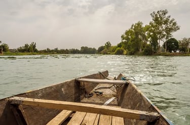 A traditional wooden boat floating on the calm Niger River with lush green trees on the banks.