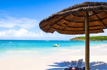 Tropical white sand beach with a thatched tiki umbrella and turquoise ocean water under a clear blue sky.