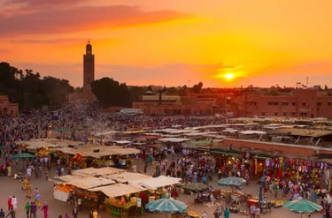 A crowded Jemaa el-Fnaa market square in Marrakech at sunset with the Koutoubia Mosque in the background.