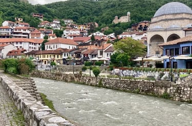 Scenic view of the Bistrica river flowing through Prizren old town with the Sinan Pasha Mosque and historic hillside houses.