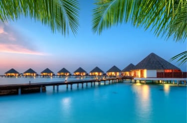 Luxury Maldives overwater bungalows at sunset with a wooden pier and palm trees.