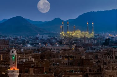 Full moon rising over the illuminated Al-Saleh Mosque and old city architecture in Sana'a, Yemen.