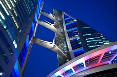 Low-angle view of the Bahrain World Trade Center towers and wind turbines illuminated at night.