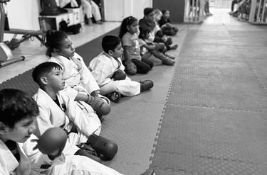 a group of kids sitting on a mat with their hands on their knees