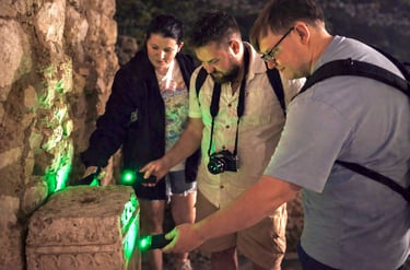 Tour participants examining ancient stone ruins with green UV lights during Athens Ghost Tour