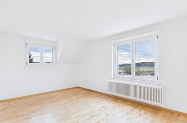 Leerer, moderner Raum mit weißen Wänden, hellem Holzboden und großen Fenstern mit Blick auf ein male