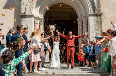 A happy bride and groom exiting a stone church while wedding guests throw colorful confetti.
