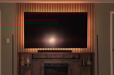 Modern wall-mounted TV with backlighting on a wood slat accent wall above a rustic fireplace console.