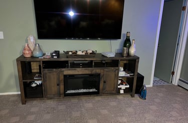 A rustic wooden TV stand with a built-in electric fireplace and decorative vases below a wall-mounted flat-screen TV.