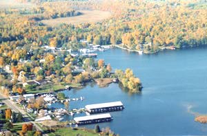 Aerial view of a boat marina on a blue lake surrounded by autumn forest trees in fall.