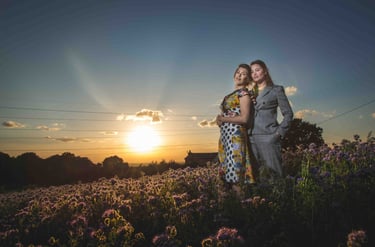 A couple poses in a field of purple wildflowers during a golden hour sunset.