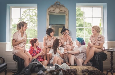 Bridesmaids in silk pajamas drinking champagne and laughing during a wedding morning bridal party.