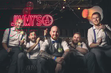 A group of happy groomsmen in suspenders celebrate at a bachelor party in a bar with confetti.