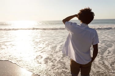 Un homme se tient debout sur la plage, contemplant l’horizon et les reflets du soleil sur l'océan.