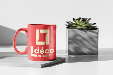 Mug en céramique rouge arborant le logo d'un décorateur d'intérieur à côté d'une plante