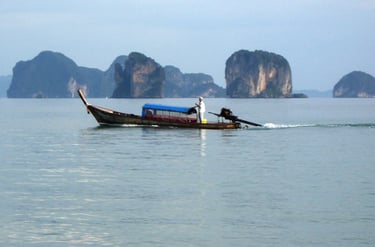 Traditional Thai longtail boat with a driver navigating calm blue water near Phuket's limestone karsts.