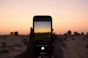 A hand holding a mobile phone in the desert at sunset