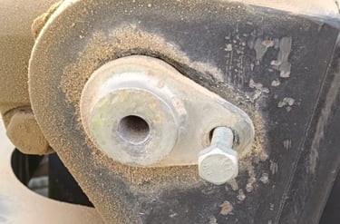 Close-up of a dusty metal pivot pin and hex bolt on heavy industrial machinery equipment.