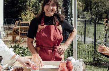 A smiling woman in a red apron prepares homemade pizza at an outdoor garden party with Mutti tomato sauce.