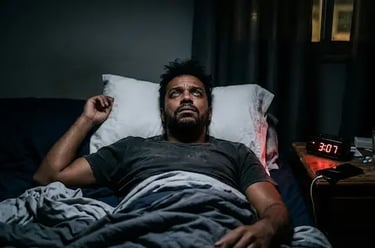 A man awake in bed at 3:07 AM suffering from insomnia and sleep deprivation symptoms.