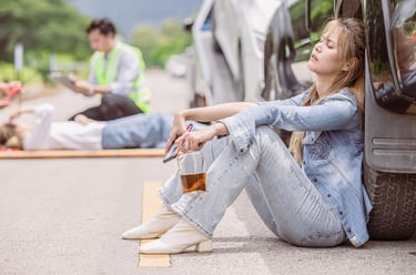 Drunk Driving incident with a woman holding a liquor bottle and sitting against a car after an accident, injured person and e