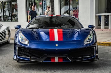 Front view of a blue Ferrari 488 Pista with red and white racing stripes parked on a city street.