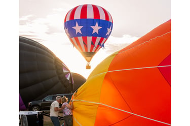 A colorful hot air balloon festival at sunrise with people preparing large balloons for flight.